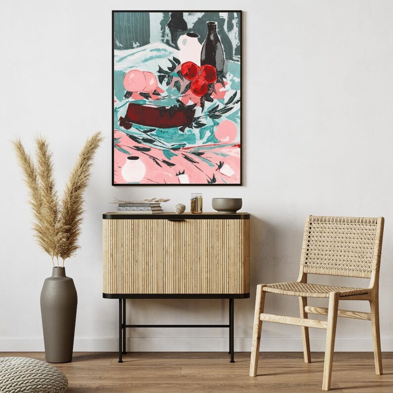 Puede incluir: Una pintura abstracta enmarcada que representa una naturaleza muerta con una botella, un jarr&oacute;n, fruta y flores sobre un mantel rosa y verde. La pintura est&aacute; colgada en una pared blanca sobre un armario de madera con un marco de metal negro.