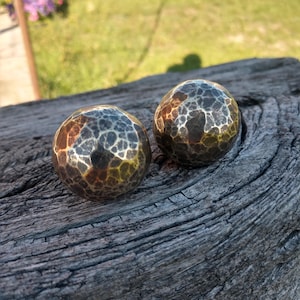 Pode incluir: Dois objetos esféricos com uma textura metálica martelada apresentando uma mistura de tons castanho-escuro, cobre e prata. As superfícies têm uma aparência facetada e reflexiva com reentrâncias visíveis nas formas arredondadas.