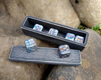 Può includere: Una scatola rettangolare in legno nero con finitura usurata contenente tre dadi iridescenti, con altri due dadi abbinati appoggiati sul coperchio separato in legno nero. I dadi presentano una finitura metallica multicolore.