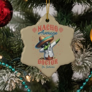 May include: A beige, star-shaped Christmas ornament with the text "NACHO Average DOCTOR" and a cartoon doctor in a sombrero doing the dab. The ornament is hanging on a Christmas tree with red and gold baubles.