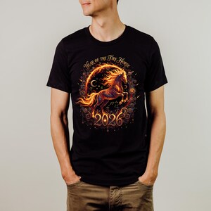 May include: Black t-shirt with a vibrant design of a fiery horse encircled by a glowing frame. The text "Year of the Fire Horse" and the year "2026" are included. The design uses orange and gold tones.