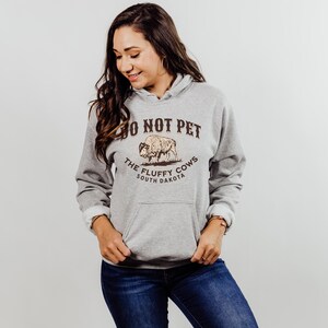 May include: A grey hooded sweatshirt with a brown graphic print of a buffalo and the text "Do Not Pet The Fluffy Cows South Dakota".