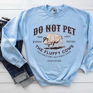 May include: Light blue sweatshirt with a graphic of a bison and the text "DO NOT PET THE FLUFFY COWS YELLOWSTONE NATIONAL PARK 8,104 FT IDAHO WYOMING MONTANA 44&deg;35'47"N 110&deg;32'50"W"