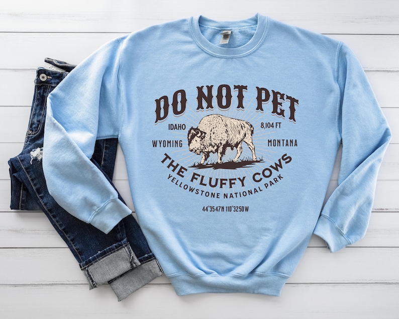 May include: Light blue sweatshirt with a graphic of a bison and the text "DO NOT PET THE FLUFFY COWS YELLOWSTONE NATIONAL PARK 8,104 FT IDAHO WYOMING MONTANA 44&deg;35'47"N 110&deg;32'50"W"