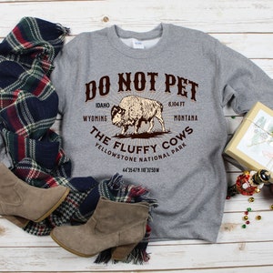 May include: Gray sweatshirt with a brown graphic of a bison and the text "DO NOT PET THE FLUFFY COWS YELLOWSTONE NATIONAL PARK 44 3547N 110 3250W 8,104 FT IDAHO WYOMING MONTANA".