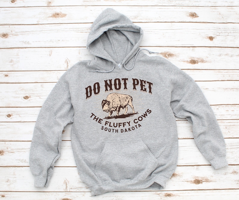 May include: Grey hooded sweatshirt with a brown graphic of a bison and the text "Do Not Pet The Fluffy Cows South Dakota".