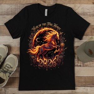 May include: Black t-shirt with a detailed illustration of a fiery horse. The design includes the text "Year of the Fire Horse 2026" and celestial elements. The horse is depicted within a circular frame, with a fiery mane and tail, creating a striking visual.