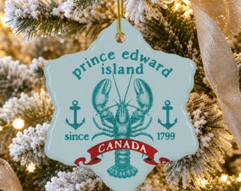Könnte beinhalten: Ein hellblaues Keramikornament mit gewelltem Rand, verziert mit einer türkisfarbenen Hummerillustration, zwei Ankern und dem Text "prince edward island since 1799" sowie einem roten Banner mit "CANADA", an einer goldenen Schnur.