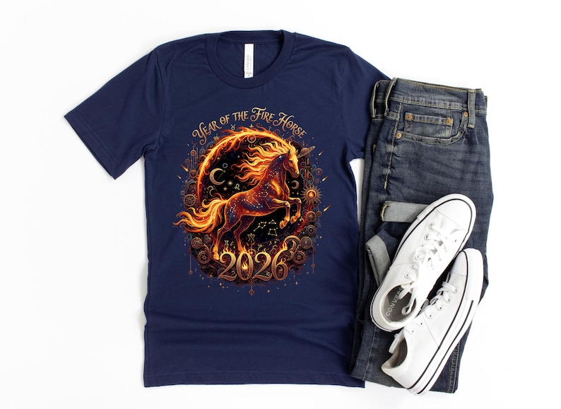 May include: A navy blue t-shirt with a fiery horse graphic, encircled by a decorative frame, and the text "Year of the Fire Horse 2026". The shirt is styled with blue jeans and white trainers for a casual look.