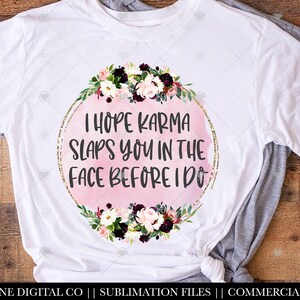 May include: White t-shirt with a pink watercolor circle and gold glitter border. The circle has the text "I hope karma slaps you in the face before I do". The circle is surrounded by a floral wreath with pink, white, and burgundy flowers.
