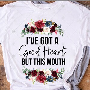 May include: White t-shirt with a floral wreath design and the text "I've got a good heart but this mouth".