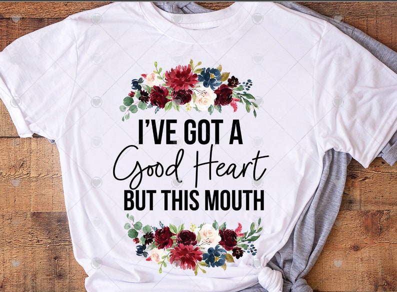 May include: White t-shirt with a floral wreath design and the text "I've got a good heart but this mouth".