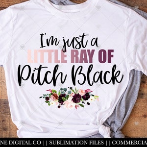 May include: White t-shirt with a black floral design and the text "I'm just a little ray of pitch black".