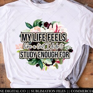 May include: White t-shirt with a floral design and the text "MY LIFE FEELS like a test I didn't STUDY ENOUGH FOR" in gold glitter lettering.