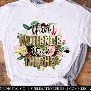 May include: White t-shirt with a floral design and gold glitter text that reads "thin patience thick thighs".