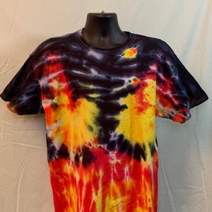 May include: A tie-dye t-shirt with a fiery design. The shirt transitions from a dark blue at the top to vibrant red and yellow at the bottom, resembling flames. The short-sleeved shirt is displayed on a black mannequin.