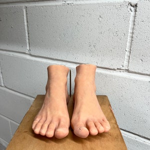 May include: A pair of realistic-looking, nude-colored, silicone feet on a wooden platform.