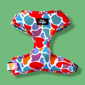 May include: A pet harness featuring a multi-colored abstract cow print pattern in red, blue, orange, and purple on a white background. The harness includes a black rectangular label with the white text full body waggle centered at the top.