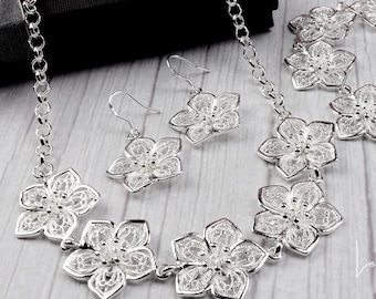 May include: A silver necklace, bracelet, and earrings set with delicate flower designs. The jewelry is made of filigree, a delicate and intricate metalwork technique.