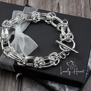 May include: A silver bracelet with a toggle clasp, displayed in a black gift box with white tissue paper. The bracelet is made of interlocking oval links.