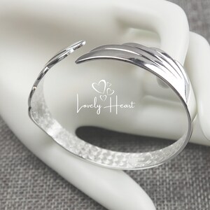 Może przedstawiać: Srebrna bransoletka z młotkowanym wykończeniem i unikalnym otwartym wzorem. Bransoletka ma fakturowaną powierzchnię i zakrzywiony kształt.