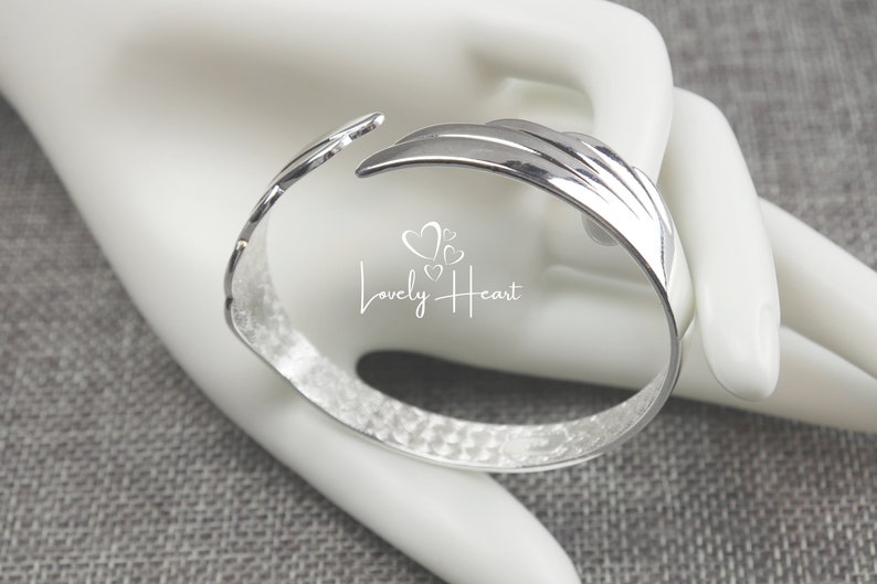 Może przedstawiać: Srebrna bransoletka z młotkowanym wykończeniem i unikalnym otwartym wzorem. Bransoletka ma fakturowaną powierzchnię i zakrzywiony kształt.