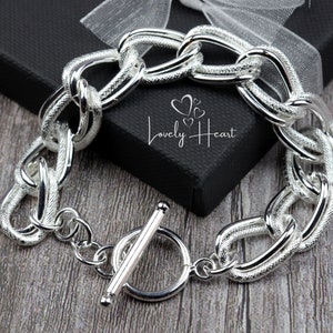 Peut inclure: Bracelet en chaîne argentée avec une finition texturée et un fermoir à glissière. Le bracelet est présenté sur une boîte noire avec le texte "Lovely Heart" dessus.