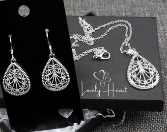 May include: A silver necklace and earrings set with a teardrop-shaped pendant and matching earrings. The pendant and earrings feature a delicate filigree design. The jewelry is displayed in a black box with the words "Lovely Heart" printed on it.