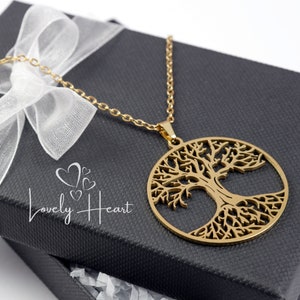 May include: A gold-toned necklace with a tree of life pendant. The pendant is a circular design with a detailed tree silhouette. The necklace is displayed in a black gift box with a white ribbon.