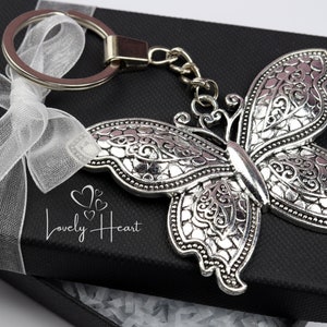 May include: A silver butterfly keyring with intricate details, presented in a black gift box with a white ribbon. The keyring features a silver ring and a silver chain.