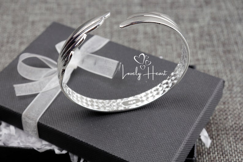 Może przedstawiać: Srebrna bransoletka typu bangle z fakturowanym, młotkowanym wykończeniem i zakrzywionym wzorem. Bransoletka jest otwarta i ma prosty, elegancki wygląd.