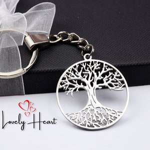 Könnte beinhalten: Silberner Schlüsselanhänger mit einem Baum des Lebens-Motiv. Der Anhänger ist an einer silbernen Kette und einem Ring befestigt und wird auf einer schwarzen Geschenkbox mit weißem Band präsentiert. Das Lovely Heart-Logo ist sichtbar.