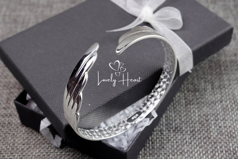 Może przedstawiać: Srebrna bransoletka typu bangle z fakturowanym wzorem. Bransoletka jest otwarta i ma zakrzywiony kształt. Bransoletka znajduje się w czarnym pudełku z białym papierem jedwabnym.