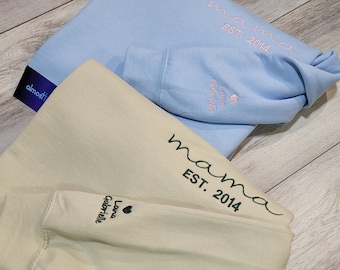 May include: Two sweatshirts, one light blue and one beige, with the text "mama est. 2014" embroidered on them. The beige sweatshirt also has the text "Lana Gabrielle" embroidered on it.