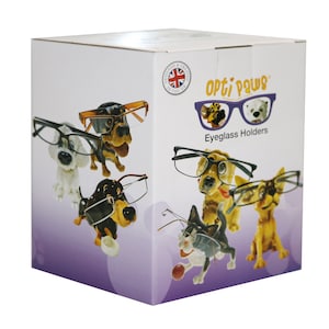 May include: A white box featuring eyeglass holders shaped like dogs wearing glasses. The box has the text "Opti Paws Eyeglass Holders" and a Union Jack logo. The eyeglass holders are various colors, including white, brown, and yellow.