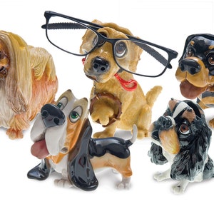 May include: A collection of ceramic dog figurines in various breeds, including a Pekingese, a Basset Hound, and a Rottweiler. One dog wears black-framed glasses. The figurines are painted with realistic details and vibrant colors.