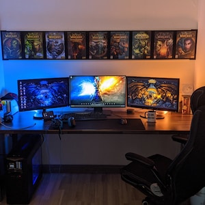 May include: A gaming setup with three monitors, a black gaming chair, and a computer tower. The monitors are displaying different images, including a dragon, a fantasy scene, and a dark background. The desk is made of wood and has a black mousepad. There are several World of Warcraft game boxes on the wall behind the monitors.