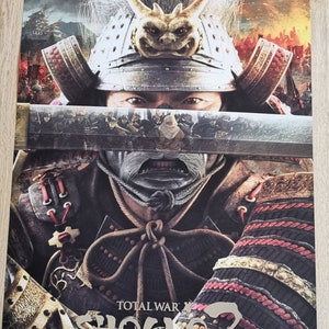 Puede incluir: Primer plano de un guerrero samur&aacute;i con un casco y una armadura tradicionales. El guerrero sostiene una espada frente a su rostro. La imagen es para el videojuego Total War: Shogun 2.