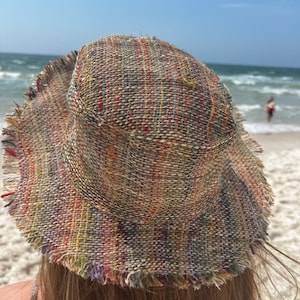 May include: A multi-colored woven bucket hat with frayed edges. The hat is made of a natural fiber and has a relaxed, bohemian style.