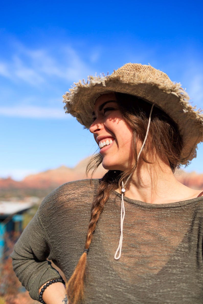 May include: A woman wearing a brown straw hat with a braided hairstyle, a green shirt, and a beaded bracelet. She is smiling and looking to the right.