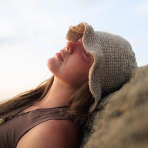 May include: A beige crochet bucket hat with a textured, woven pattern and a slightly wavy, flexible brim. The hat is crafted from a light-colored yarn, featuring a dense, uniform stitch construction that provides a structured yet soft appearance.
