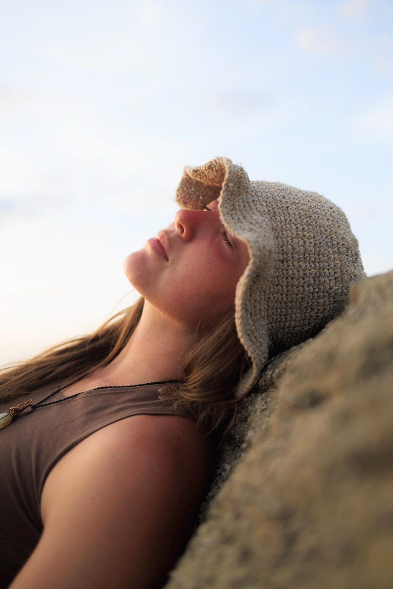 May include: A beige crochet bucket hat with a textured, woven pattern and a slightly wavy, flexible brim. The hat is crafted from a light-colored yarn, featuring a dense, uniform stitch construction that provides a structured yet soft appearance.