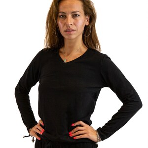 May include: A black long-sleeved shirt with a v-neck and a silver necklace. The person is wearing a silver hoop earring.
