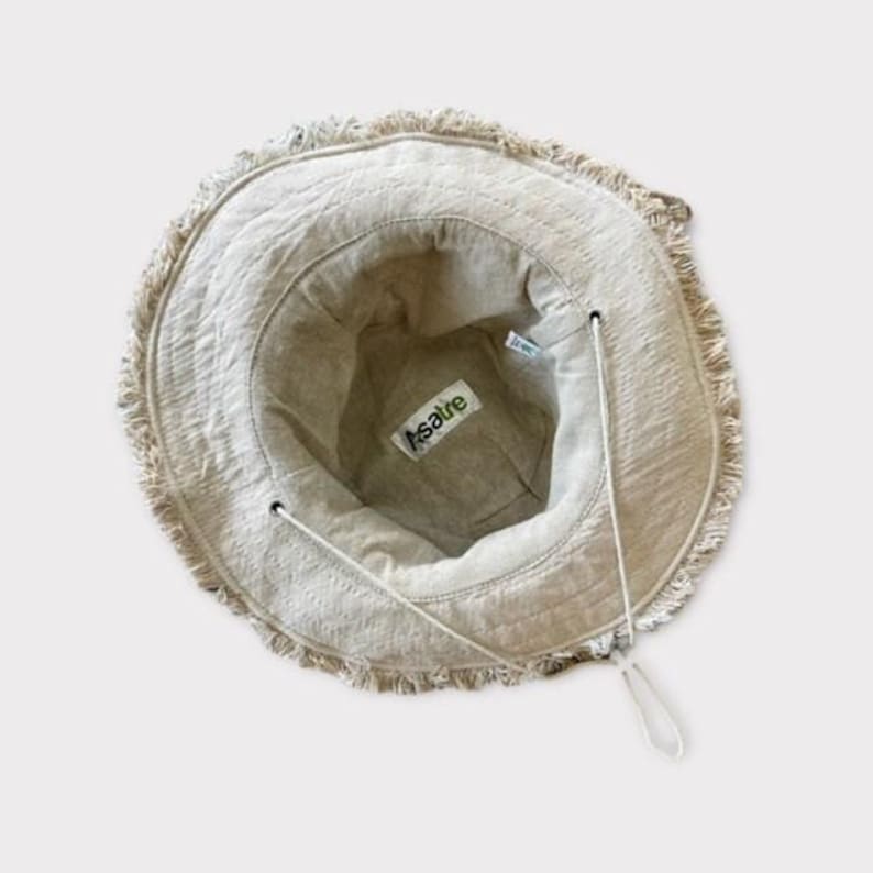 May include: A beige linen bucket hat with a frayed edge and a green and white "Asatre" label inside.