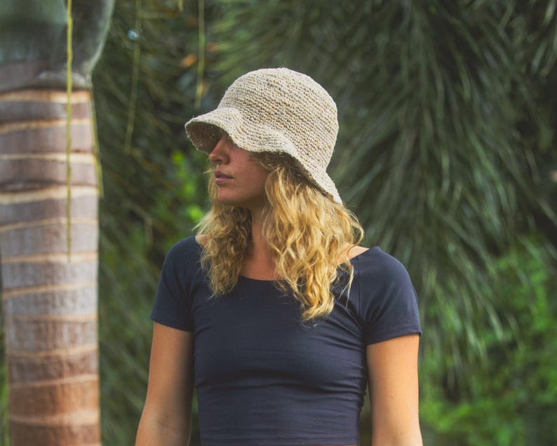 May include: A beige crochet bucket hat with a textured, woven appearance and a slightly flared brim. The hat features a natural, fibrous material construction with a visible knit pattern, providing a structured yet flexible shape for the head.