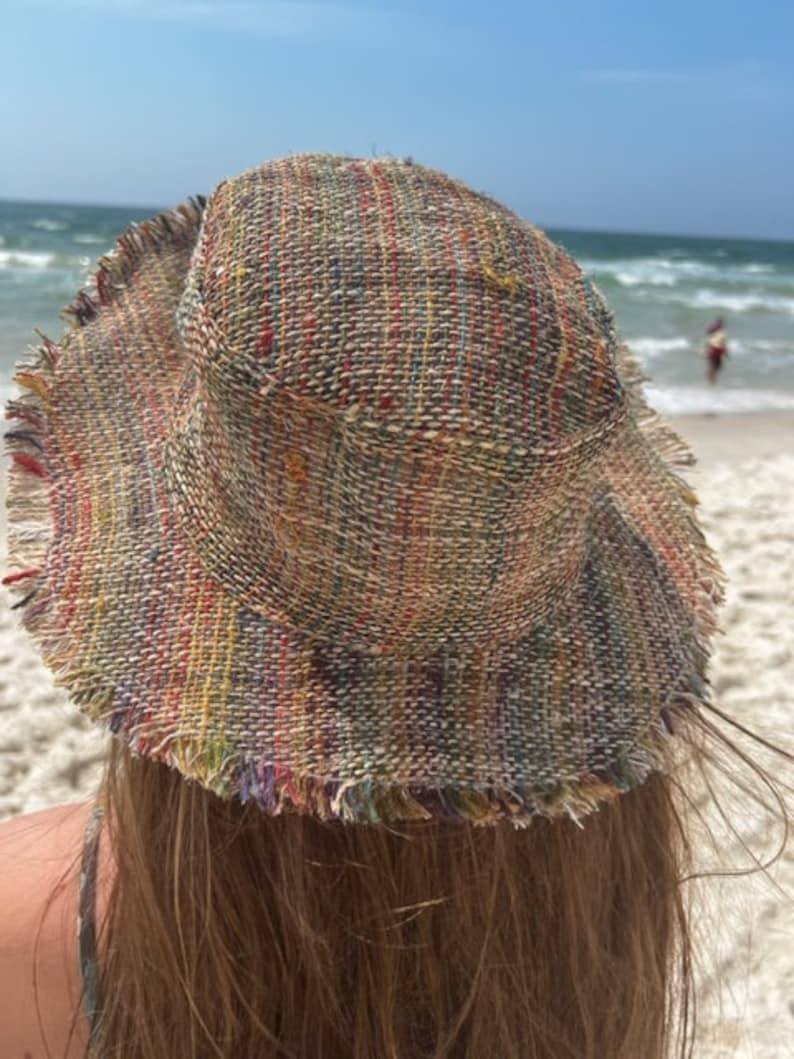 May include: A multi-colored woven bucket hat with frayed edges. The hat is made of a natural fiber and has a relaxed, bohemian style.
