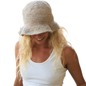 May include: A beige crochet bucket hat with a textured, speckled yarn finish and a slightly flared brim. The hat features a dense, hand-knitted construction with a neutral color palette, showcasing a rounded crown and a soft, flexible brim structure.
