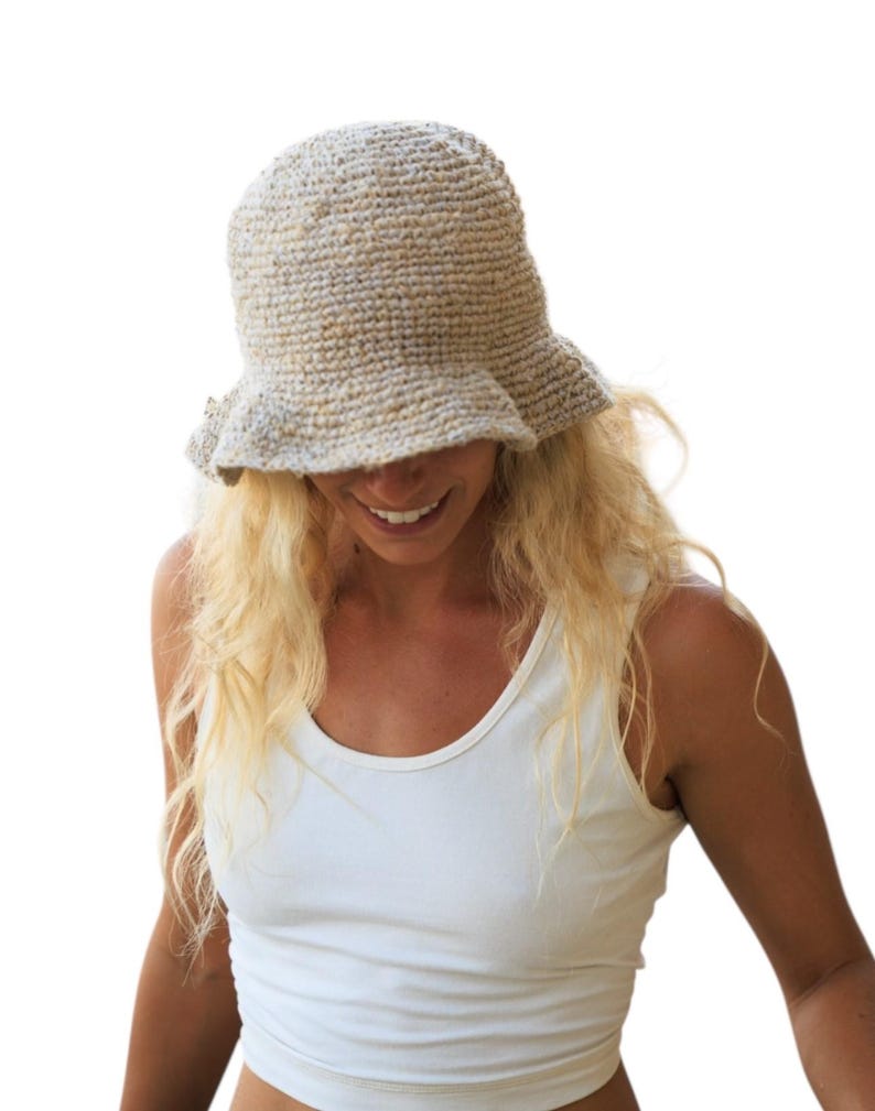 May include: A beige crochet bucket hat with a textured, speckled yarn finish and a slightly flared brim. The hat features a dense, hand-knitted construction with a neutral color palette, showcasing a rounded crown and a soft, flexible brim structure.