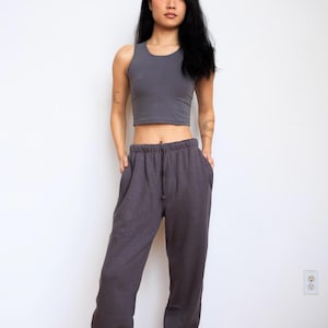 May include: A dark gray sleeveless crop top with a round neckline paired with matching dark gray loose-fitting sweatpants featuring an elastic waistband and a drawstring. The set is made of a solid-colored fabric with a consistent matte texture.