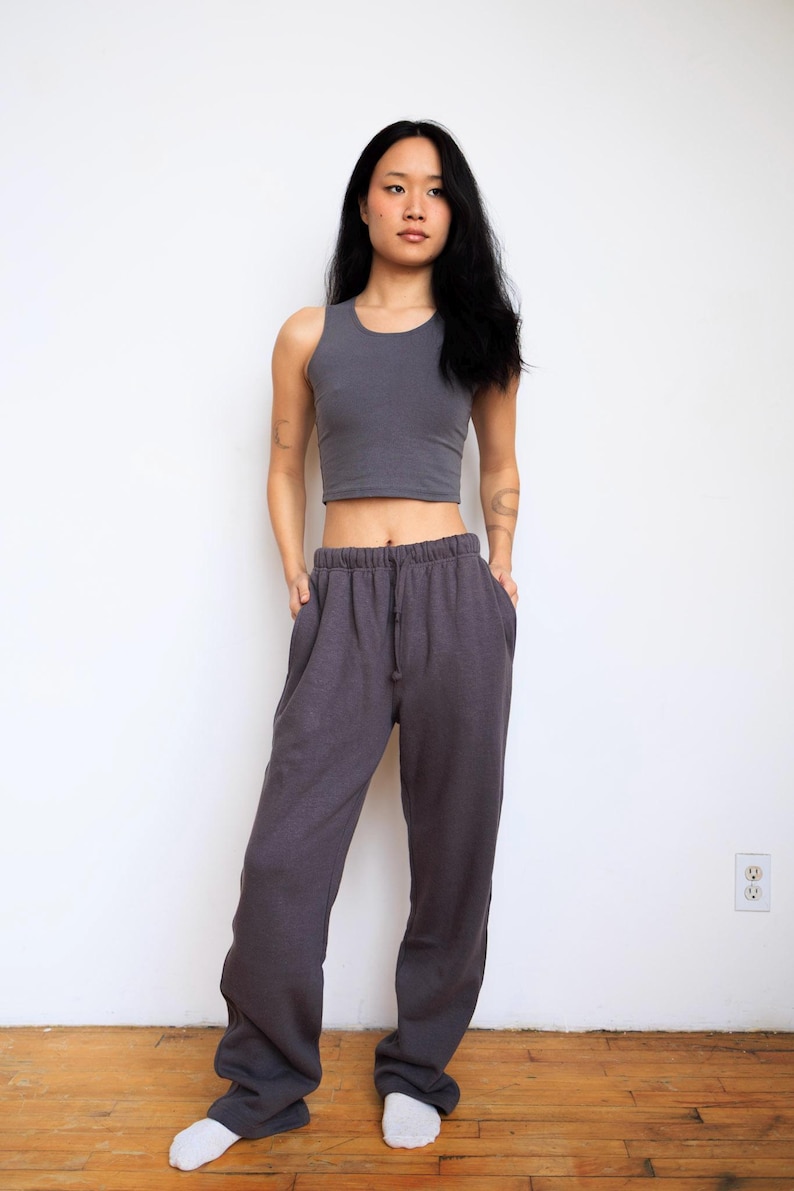 May include: A dark gray sleeveless crop top with a round neckline paired with matching dark gray loose-fitting sweatpants featuring an elastic waistband and a drawstring. The set is made of a solid-colored fabric with a consistent matte texture.